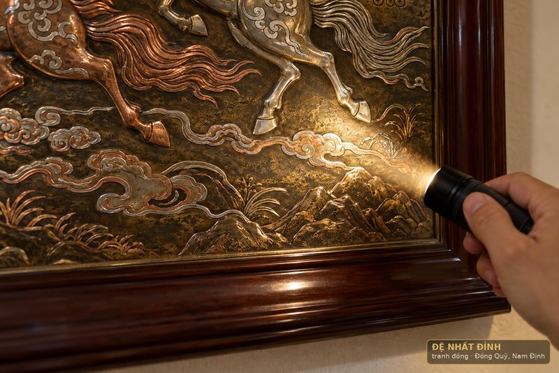 Ảnh minh hoạ: góc tranh đồng khảm tam khí dưới ánh sáng xiên, rãnh khảm bạc và đồng đỏ nổi rõ đường ranh kim loại